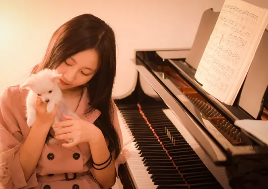 犬を抱っこしてピアノの前に座っている女性